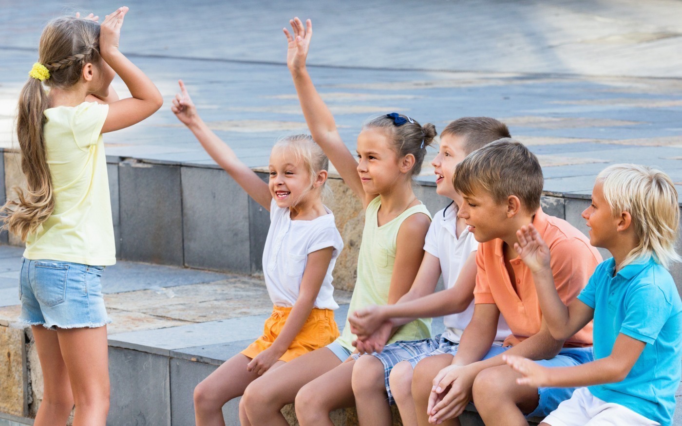 A youth standing with hands to ears facing group of five others that are guessing what animal the child is acting out.