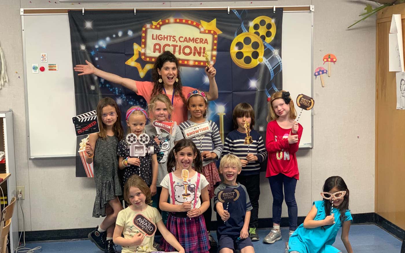 Teacher posing with a group of her students holding theater props