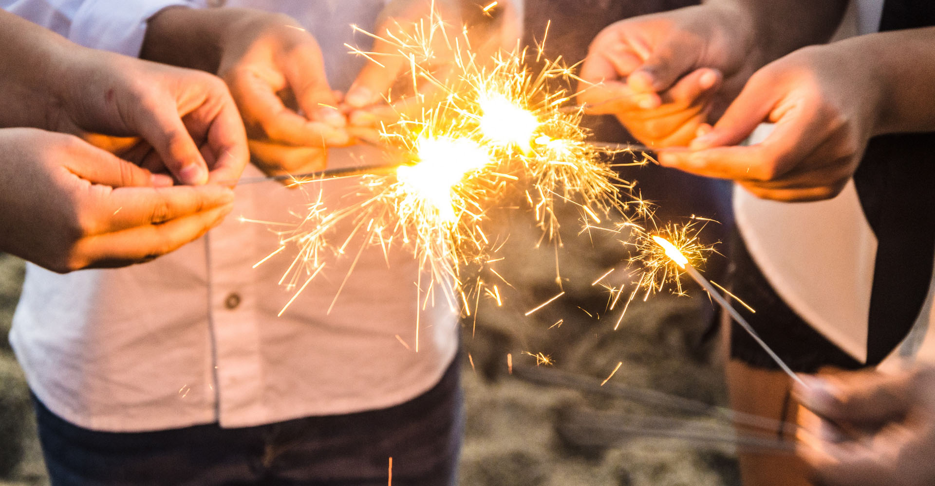 Hands holding lit sparklers touching in the center