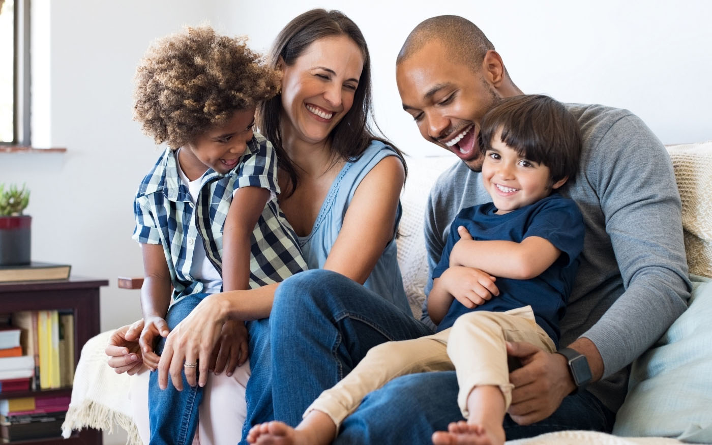 A family of four laughing and playing on a couch