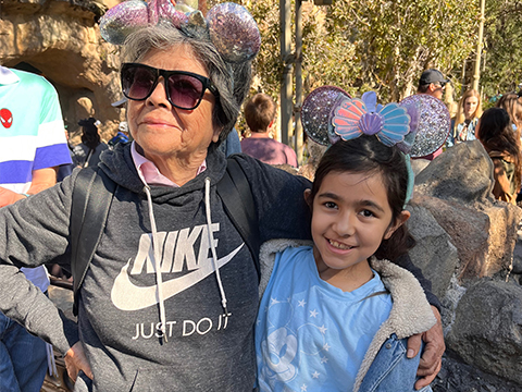 Grandma with arms around granddaughter are proudly posing wearing matching glittery mouse ears.