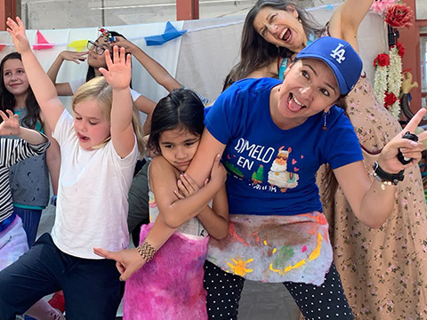 Small group of campers and teachers making funny poses for the camera during a dance performance, and in the front a young child grimaces while holding onto the arm of her teacher.