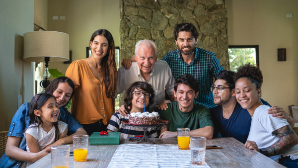 A multi-generational family of 9 celebrating a birthday around the dining table with cake and gifts